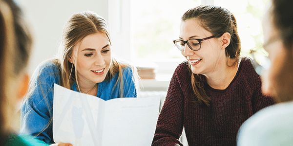 Two young women looking at class work