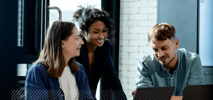 Three smiling people looking at computers together