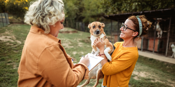 woman filling out a form on a clipboard while another woman holds up a dog to adopt