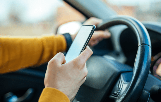 Persona behind the wall of a car holding a cell phone while driving