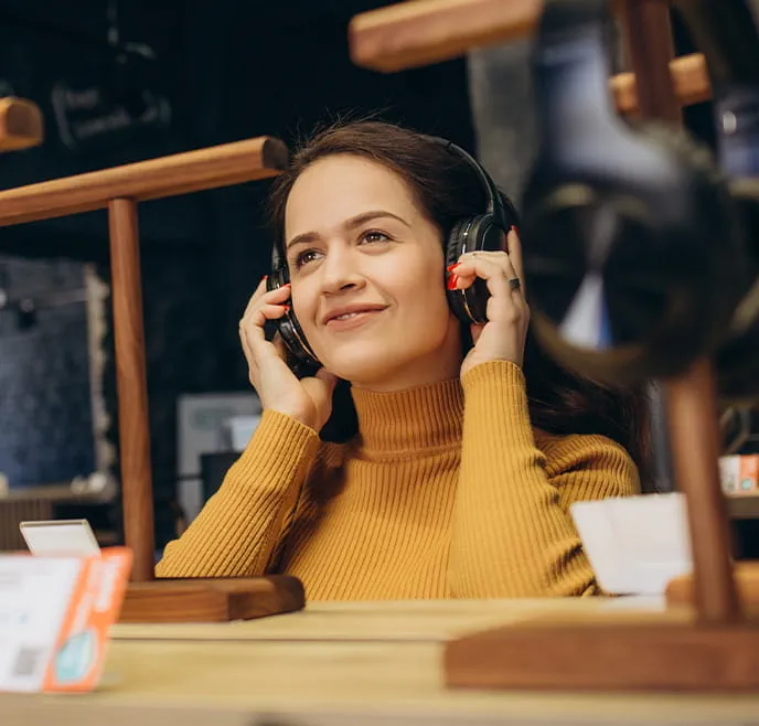 Smiling woman in an orange sweater with over-the-ear headphones