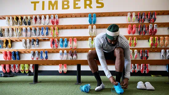 Man sitting on a bench in front of a wall of shoes trying on shows. 