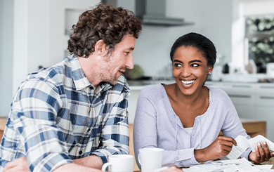 Mana and woman sitting at a table with coffee mugs in front of them. The woman is holding pieces of paper in her hands.