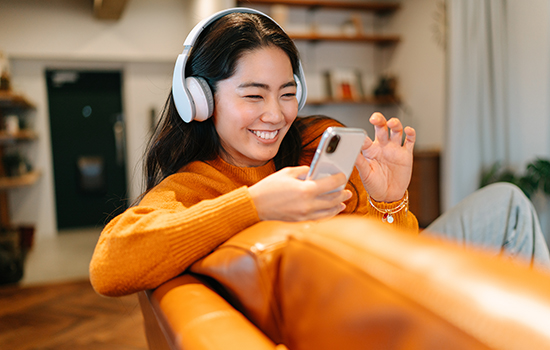 Smiling woman on couch with headphones and a mobile phone listening to a podcast