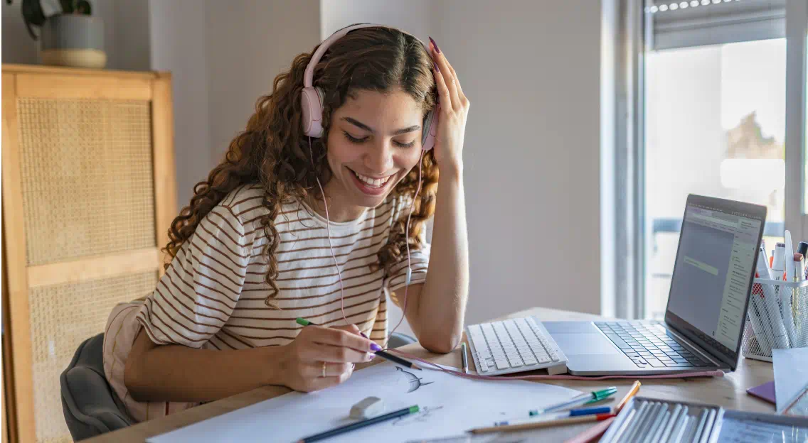 Young woman wearing headphones at a desk with paperwork and a laptop