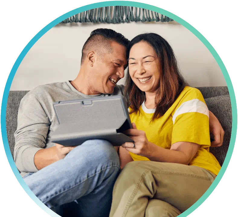 Couple using a tablet, sitting on a couch and laughing