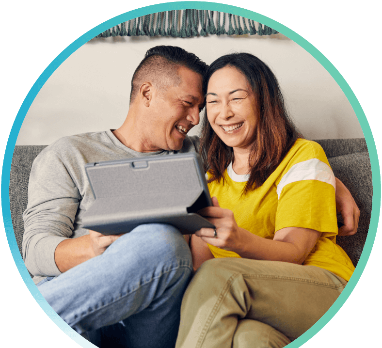 Couple using a tablet, sitting on a couch and laughing