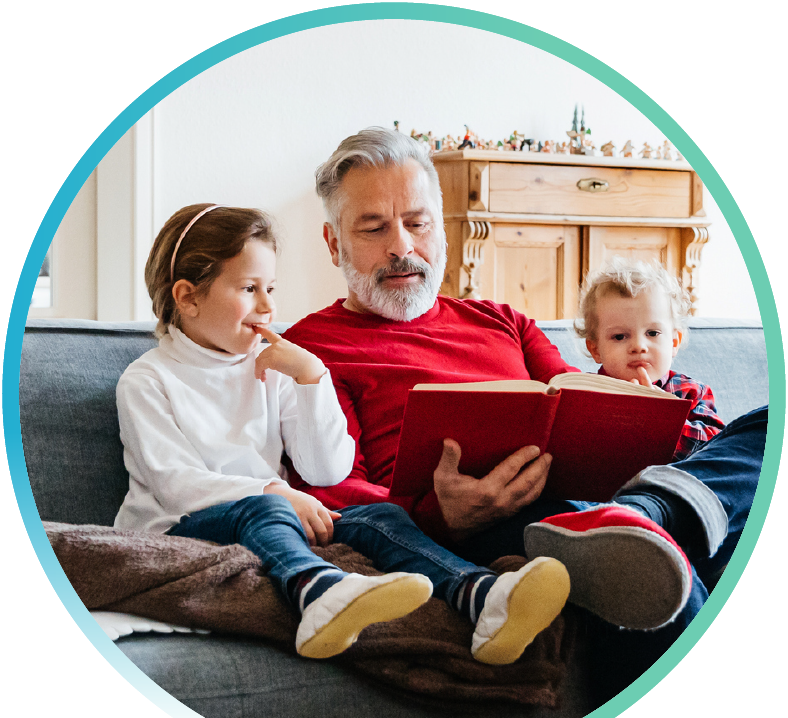 Man reading a book to two children on a sofa.