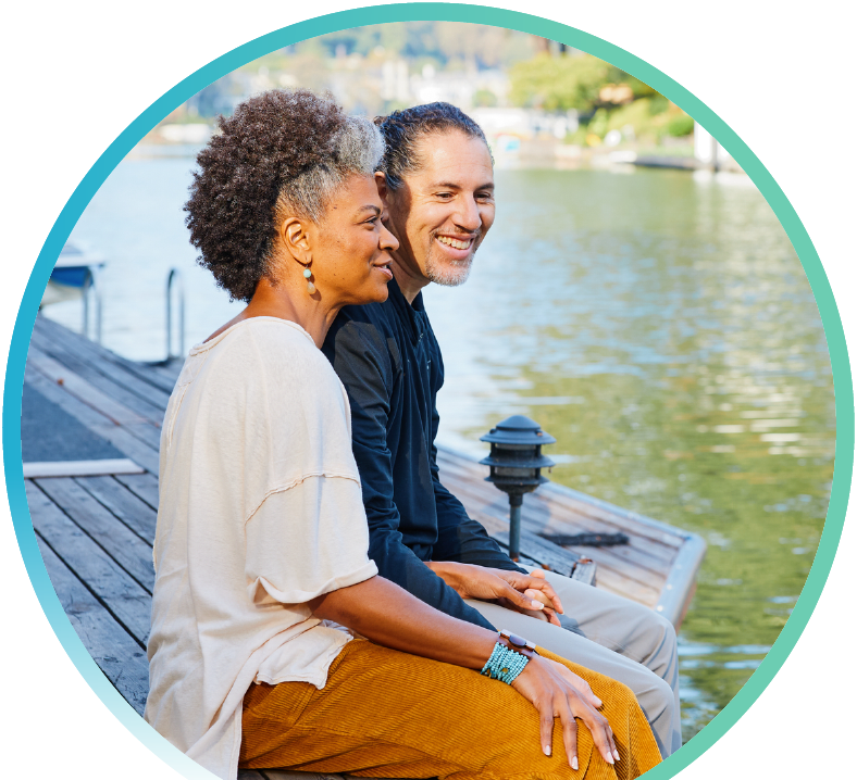 Two people holding hands while dangling their feet on a pier overlooking water.