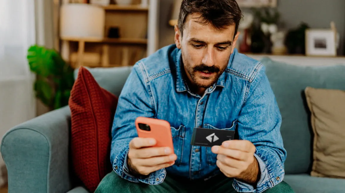 Dark-haired man in a blue shirt holding a mobile phone and a credit card