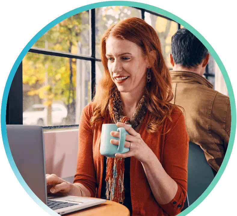 Image of a woman sitting in a coffee shop, with a coffee mug in hand, and working on their laptop.