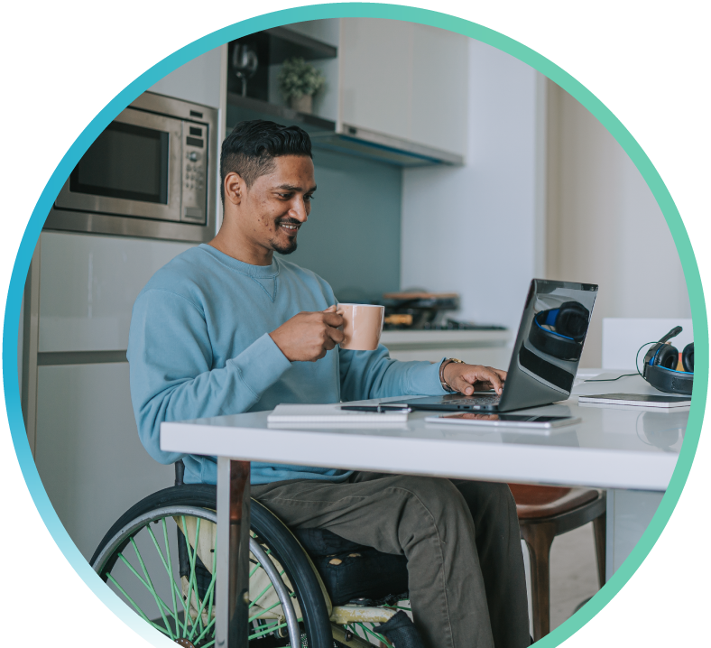 Man doing some work on a laptop, holding a mug in one hand. There is a kitchen setting in the background.