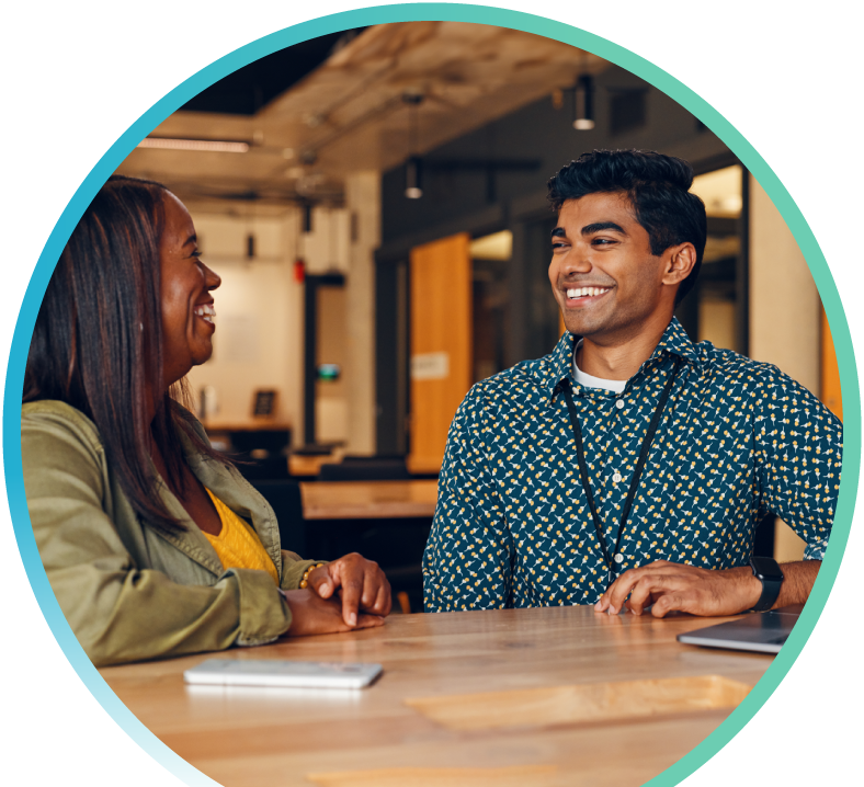 I man wearing an ID badge around his neck is sitting with a woman at a table in an office setting.