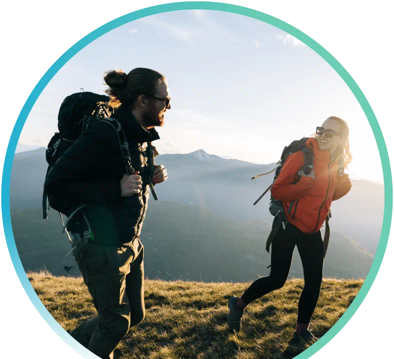 Man and a woman hiking in a grassy/mountain setting while carrying backpacks.