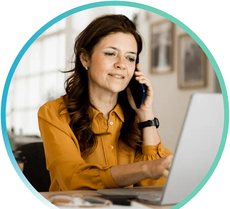 Woman holding a phone to her left ear while typing on an open laptop with her right hand.