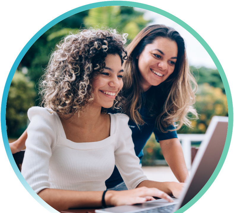 A prospective college student is sitting outside with a laptop open in front of her with her mother looking over her shoulder.