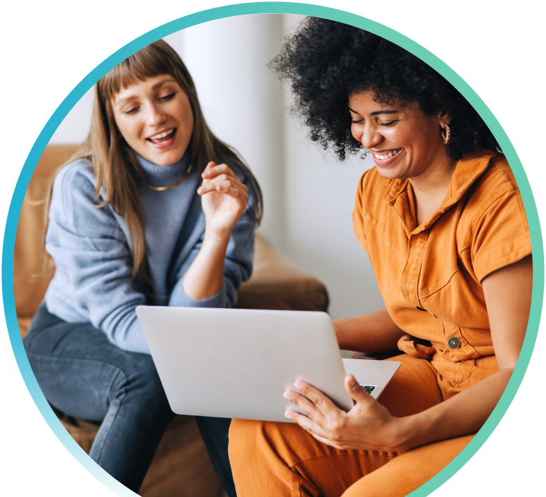 Two women witting on sofas and looking at an open laptop screen.