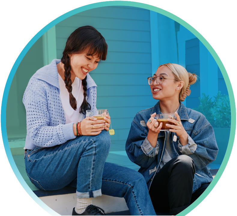 Two women sitting on a porch with cups of tea in their hands.