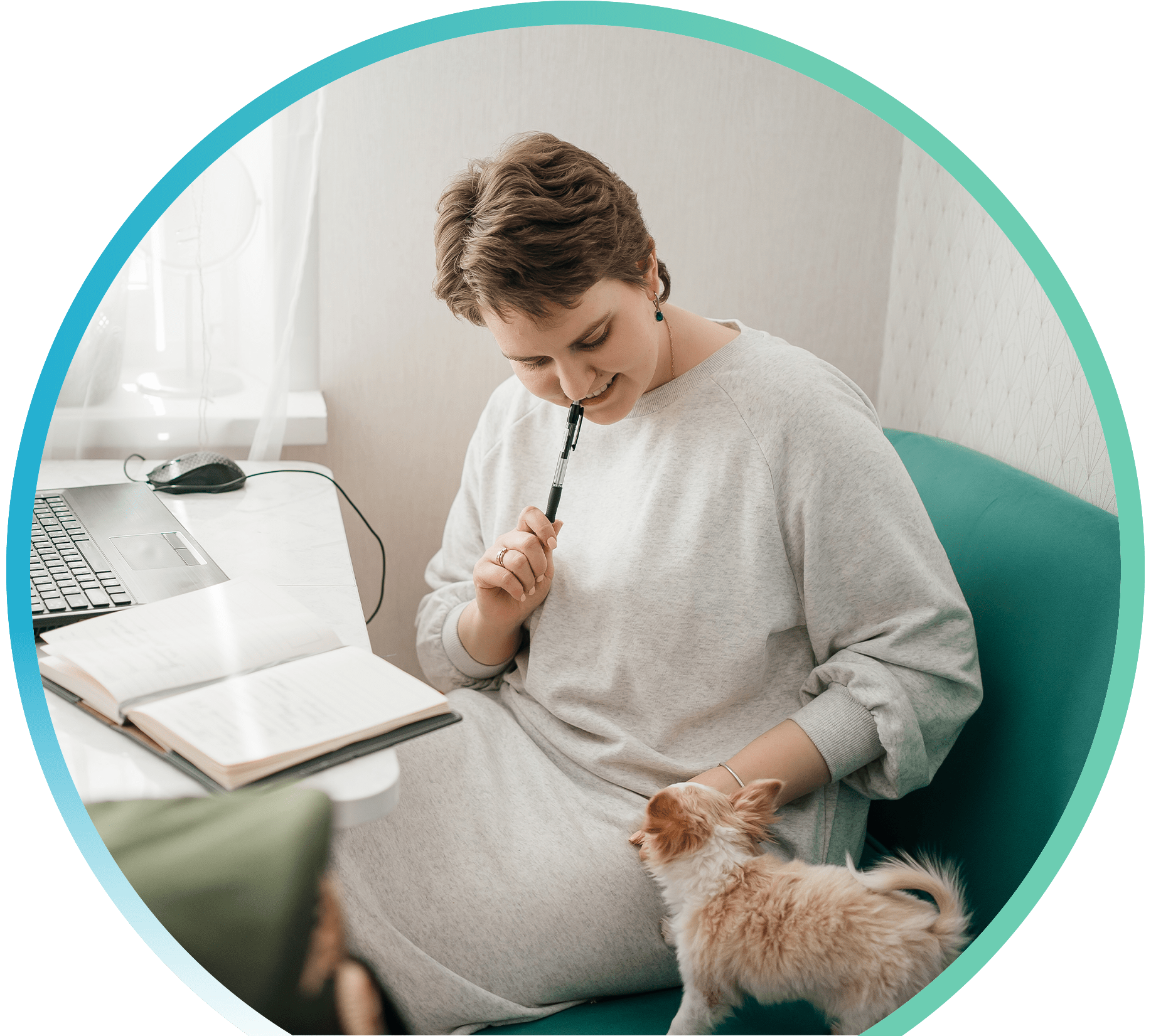 Woman at a table with a laptop and notebook, looking down at a small dog.