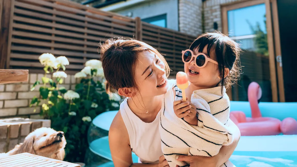 Woman and little girl with pink sunglasses by the pool with their dog.