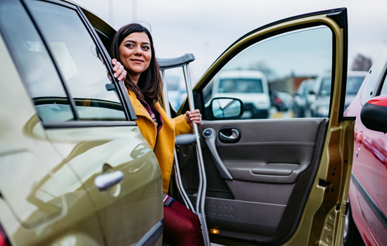 A woman is getting out of the passenger side of a car holding crutches in one hand.