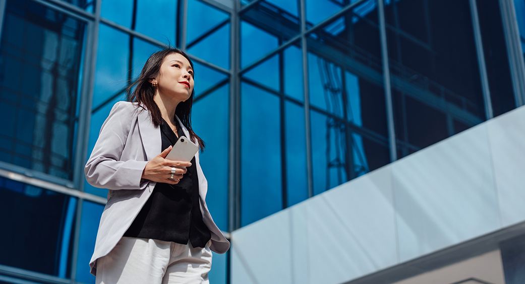 Woman outside office building in business clothing holding a mobile phone.